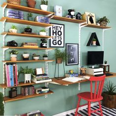 a desk with books, plants and pictures on the wall above it is also a red chair