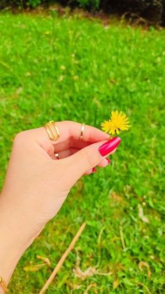 a woman's hand holding a yellow flower in the middle of her fingers,