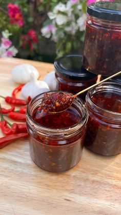 three jars filled with chili sauce sitting on top of a cutting board next to peppers