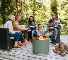 a group of people sitting around a fire pit on top of a wooden deck next to trees