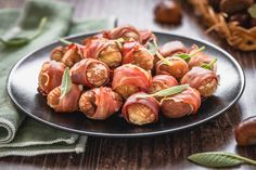 a black plate filled with bacon wrapped in green leafy garnish on top of a wooden table