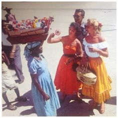 three women in dresses are carrying baskets on their heads and one woman is holding a basket