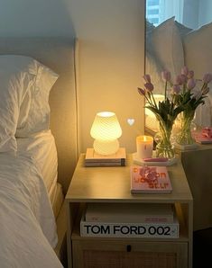 a bedside table with flowers on it and a lamp next to the night stand in front of them