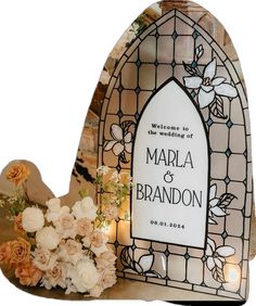 a candle holder with flowers and candles in front of a stained glass window that reads, welcome to the wedding of marla & brandon