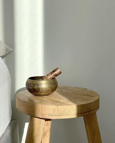 a small wooden stool with a bowl on it and a pillow in the back ground