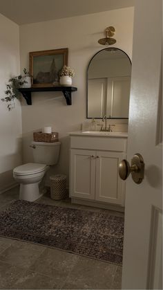 a white toilet sitting next to a sink in a bathroom under a mirror and shelf