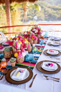 the table is set with colorful flowers and place settings for an outdoor dinner or party