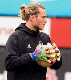 a man holding a soccer ball in his right hand and wearing gloves on the other