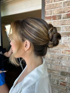 a woman standing in front of a brick wall with her hair styled into a low bun