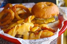 a cheeseburger and onion rings on a red plate with paper napkins in front of it