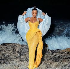 a woman in a yellow dress standing on rocks