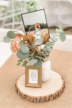 a vase filled with flowers and greenery on top of a wooden table next to a photo frame