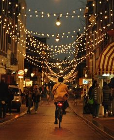 a person riding a bike down a street with lots of lights strung over the buildings