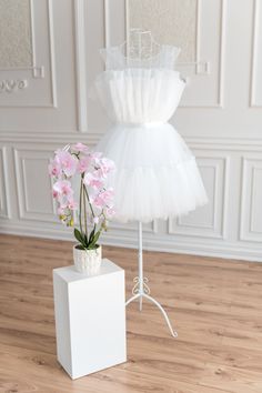 a white dress on a mannequin with pink flowers in the vase next to it