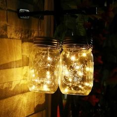 two mason jars with lights hanging from them on the side of a building at night