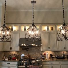 three lights hanging from the ceiling above a stove top oven in a kitchen with white cabinets