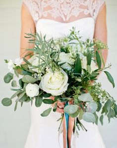 a bride holding a bouquet of flowers and greenery