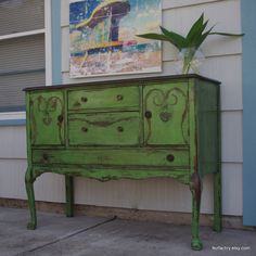 an old dresser painted green in front of a house with a painting on the wall