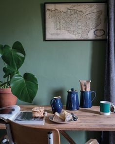 a wooden table topped with blue and green coffee cups next to a potted plant