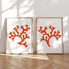 two framed pictures with orange corals on them in front of a white wall and wooden floor