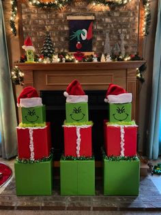 three green and red wrapped presents sitting in front of a fireplace with christmas decorations on it