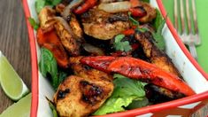 a salad with chicken and peppers in a red bowl next to a lime wedge on a wooden table