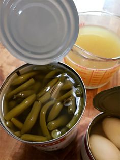 two tins filled with pickles and eggs next to an empty container full of liquid