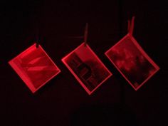 three pictures hanging on a clothes line in the dark with red light coming from them