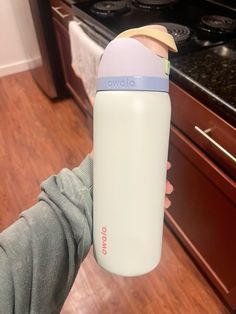 a person holding a white and blue water bottle in front of a stove top oven