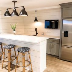 a kitchen with three stools next to an island in front of a refrigerator and microwave