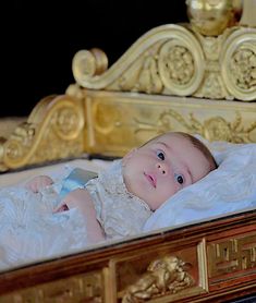 a baby laying on top of a bed next to a golden headboard and mirror