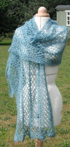 a white mannequin wearing a blue crochet shawl on top of a grass covered field