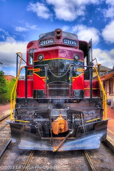 a red and black train engine sitting on the tracks next to a building with blue skies in the background