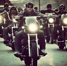 a group of men riding motorcycles down a street with their headlights turned to the side