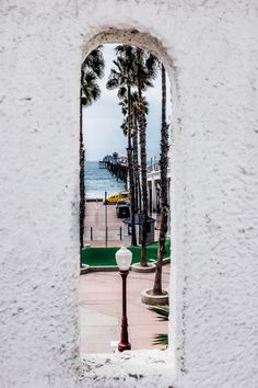 a white wall with a street light and palm trees in the background, seen through a window