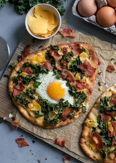 two pizzas with eggs and spinach on them next to some other food items