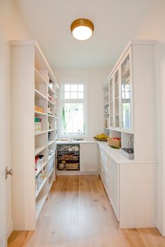 a narrow kitchen with white cabinets and wood flooring on the walls, along with open shelving units