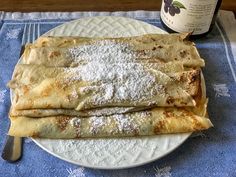 two crepes on a plate with powdered sugar and a bottle of wine