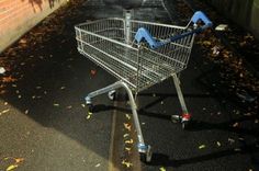 an empty shopping cart sitting on the side of a road next to a brick wall