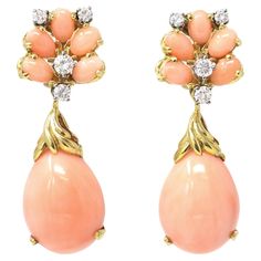 A rare vintage pair of dangling earrings signed La Triomphe CA 1980. The earrings feature natural Angelskin coral drop pendants with intricate gold design. The coral pendants hang from a cluster of the same coral and diamond tops. The handmade earrings are set in 18 karat yellow gold with an estimated 0.90 carats of diamonds GH color and VS clarity. The gross weight is 20.7 grams. The earrings measure 0.96” long. Coral Earrings Dangle, Coral Pendants, Diamond Dangling Earrings, Diamond Tops, Coral Pendant, Coral Earrings, Dangling Earrings, Drop Pendant, Earrings Dangle