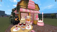 two people are sitting at a table in front of a small pink house with cakes and cupcakes on it