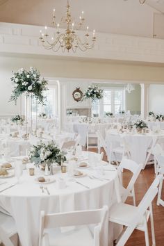 a room filled with lots of white tables covered in white linens and flowers on top of them