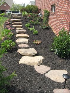 a stone path in the middle of a garden next to a brick building and flowers