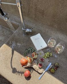 an open book sitting on top of a table next to some fruit and wine glasses