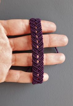 a hand is holding a purple bracelet with holes in the middle and two fingers are next to it