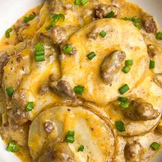 a white bowl filled with potatoes covered in cheese and meat sauce, garnished with green onions