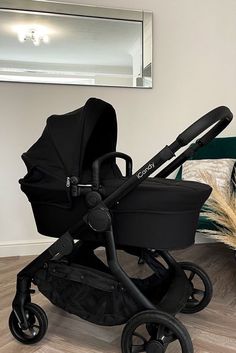 a black stroller sitting on top of a hard wood floor next to a mirror