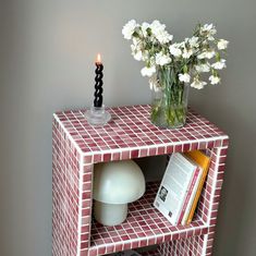 a vase filled with flowers sitting on top of a red and white shelf next to a book