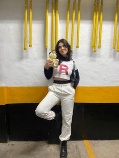 a woman holding a teddy bear in front of a wall with yellow poles on it