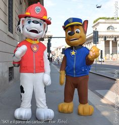 two cartoon characters are standing on the side walk near a building and one is wearing a fireman's hat